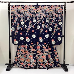 May include: A dark navy blue kimono featuring an intricate all-over pattern of red, white, and gold floral motifs, including plum blossoms and stylized pine trees. The garment is displayed on a black wooden stand with decorative inlay details.