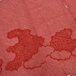 Puede incluir: Tela roja con un patrón texturizado y un diseño estilizado rojo más oscuro. La tela parece ser un kimono o una prenda similar, con costuras visibles y un borde doblado. El diseño es abstracto.