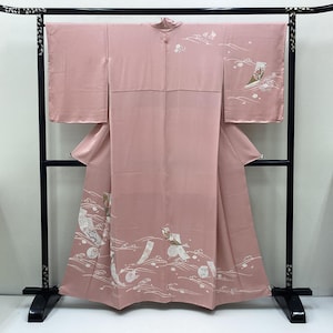 May include: A dusty pink kimono featuring white and muted floral patterns along the lower hem and sleeves. The garment displays delicate wave motifs and small rectangular accents, showcasing a traditional T-shaped silhouette with wide sleeves.