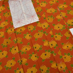 Peut inclure: Kimono orange avec un motif répété de fleurs jaunes et de feuilles vertes. Le col est blanc avec un motif de toile d'araignée rouge. Le kimono est fait d'un tissu léger.