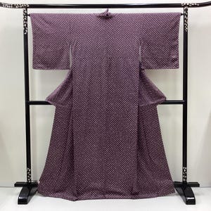 Puede incluir: Un kimono morado con un estampado de lunares blancos se exhibe en una percha negra. El kimono tiene mangas anchas y una falda larga y fluida. La percha tiene detalles decorativos en la parte superior e inferior.