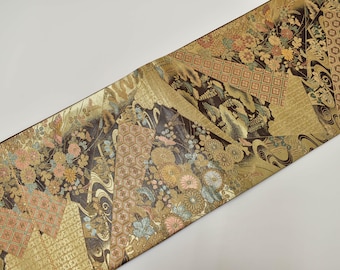 May include: A decorative textile with a patchwork design featuring floral and geometric patterns in gold, brown, and pastel colors. The fabric has a metallic sheen and is likely used for decorative purposes.