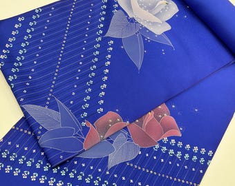 May include: A vibrant blue fabric with a floral pattern. Large white and red roses are printed on the fabric, along with smaller white floral accents and diagonal lines. The fabric is rolled up in the upper right corner.