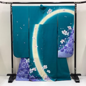 May include: A teal kimono featuring a large, curved cream-colored band across the center. The garment is decorated with scattered white and pink cherry blossom motifs, with a gradient of purple floral patterns at the lower left and right sleeves.