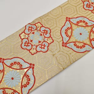 以下が含まれることがあります： 金とベージュの背景に、赤と水色の花柄が繰り返される装飾的な織物。生地は六角形のパターンで、衣類や室内装飾に使用される可能性があります。