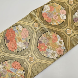 May include: A decorative runner with a repeating pattern of floral medallions in shades of peach, pink, and white, set against a gold and olive green background. The runner features a geometric design with gold accents.