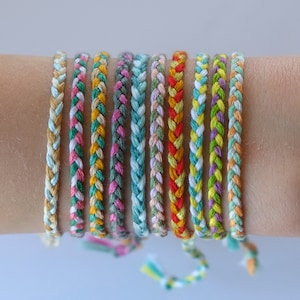 May include: A stack of colorful friendship bracelets made with braided string. The bracelets are in various colors, including green, yellow, orange, pink, and blue.