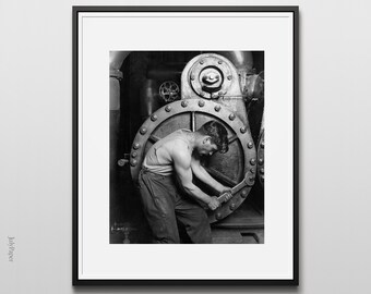 Könnte beinhalten: Ein Schwarzweißfoto eines Mannes, der an einer großen Industriemaschine arbeitet. Er trägt ein ärmelloses Hemd und eine Hose und verwendet einen Schraubenschlüssel, um eine Schraube festzuziehen.