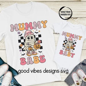 Puede incluir: Camisetas blancas y un body de bebé con un diseño de Halloween Mummy Babe. El diseño presenta una momia de dibujos animados sosteniendo una calabaza, con las palabras "Mummy Babe" en fuente retro. La imagen incluye el texto "good vibes designs svg".