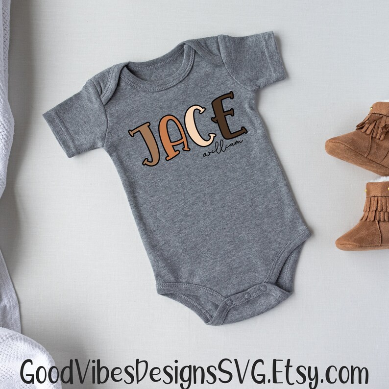 Puede incluir: Un body de beb&eacute; gris con el nombre "Jace William" escrito en letras marrones, naranjas y beige.
