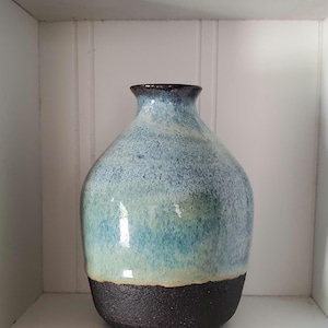 May include: A handcrafted ceramic vase with a rounded body and a narrow neck. The vase features a gradient of colors, transitioning from a dark brown base to shades of blue and turquoise, with a dark brown rim. The vase is a decorative item.