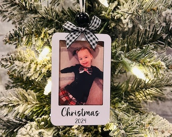 Puede incluir: Adorno de foto blanco con un lazo a cuadros blanco y negro. El adorno tiene una foto de un niño pequeño con una camisa a cuadros rojo y negro y una corbata de moño negra. El texto "Christmas 2024" está impreso en el adorno.