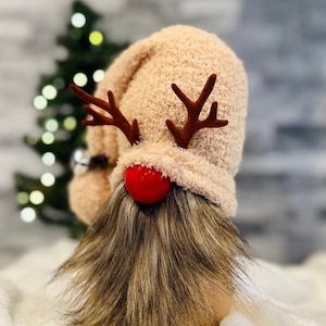 May include: A plush gnome with a pink fuzzy hat, red reindeer antlers, and a red pom-pom nose. The gnome has a long brown and gray beard.