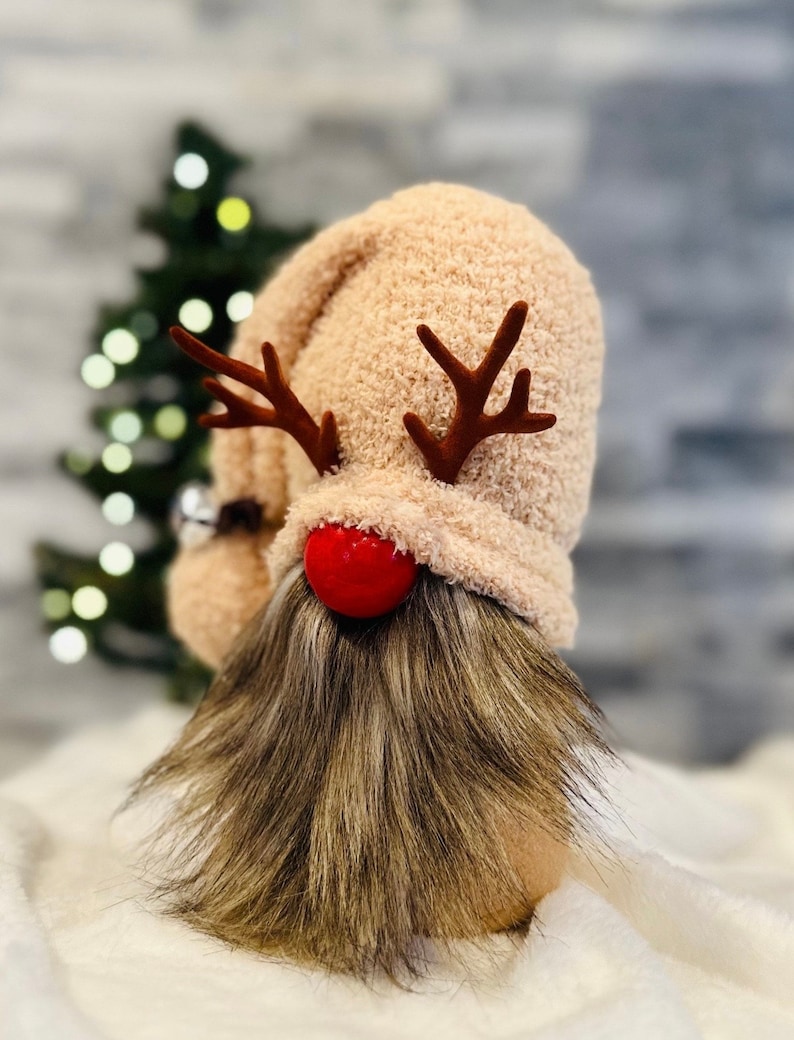May include: A plush gnome with a pink fuzzy hat, red reindeer antlers, and a red pom-pom nose. The gnome has a long brown and gray beard.