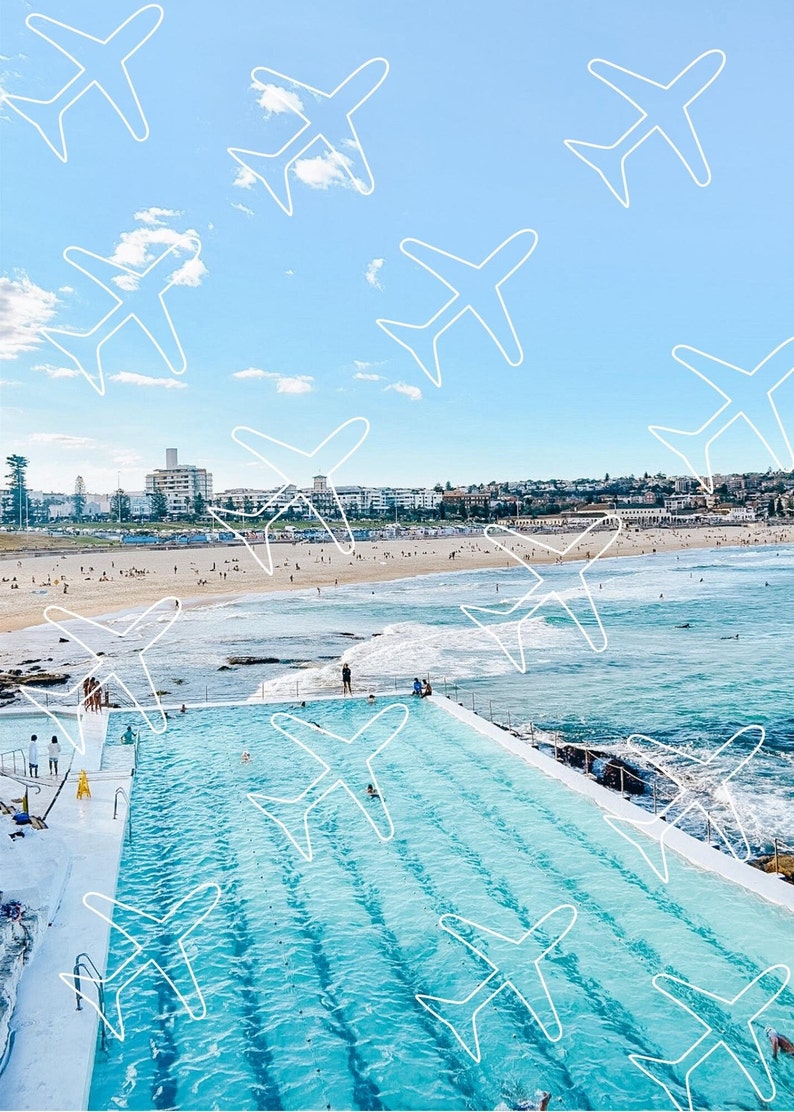 May include: An aerial view of a large outdoor swimming pool with a city skyline in the background. The pool is surrounded by a concrete deck and is filled with clear blue water. The sky is a bright blue with white clouds. There are white outlines of aeroplanes drawn on the sky.