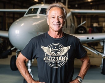 May include: A man wearing a black t-shirt with a vintage-style graphic of a plane with the text "N123AB". He is standing in front of a small airplane.