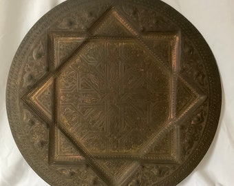 May include: A large, round, brass tray with an intricate, embossed design. The design features a central star shape surrounded by geometric patterns.