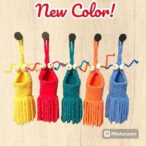 May include: Five crocheted hanging bird feeders in yellow, pink, teal, orange, and blue with white googly eyes and a whimsical design.  "New Color!" is written in red at the top of the image.