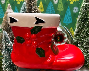 May include: A red ceramic Santa boot with green holly and berries. The boot is a Christmas decoration and can be used as a planter.