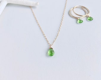 May include: A delicate gold chain necklace with a small green gemstone pendant. Matching green gemstone earrings dangle from gold hoops.
