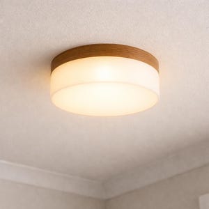 May include: A circular flush-mount ceiling light with a wood-effect trim and a frosted glass shade. The light emits a warm glow. The fixture is designed for indoor use and is mounted on a white ceiling.