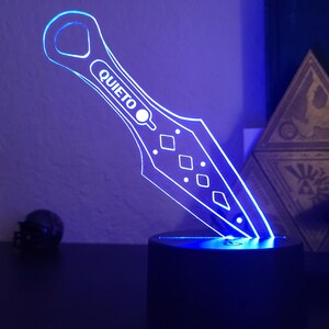 May include: A blue LED light shaped like a knife with the word "QUIETO" on it. The light is on a black base.