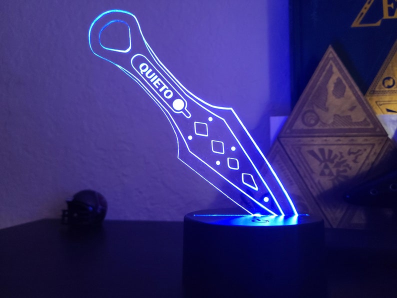 May include: A blue LED light shaped like a knife with the word "QUIETO" on it. The light is on a black base.