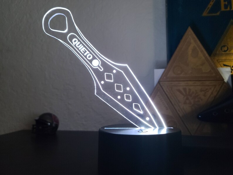 May include: A white acrylic knife-shaped night light with the word "QUIETO" on the handle. The light is on a black base.
