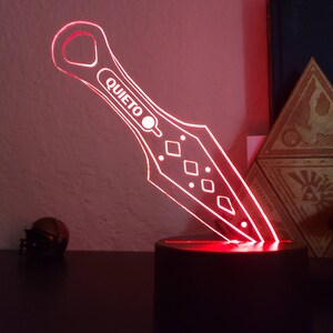 May include: A red illuminated acrylic knife with the word "QUIET" on it. The knife is on a black base and is lit from below.