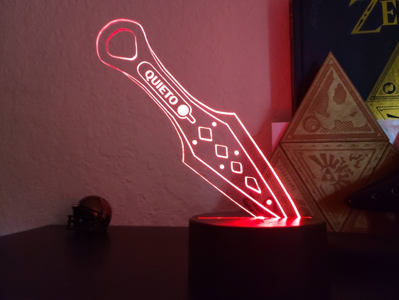 May include: A red illuminated acrylic knife with the word "QUIET" on it. The knife is on a black base and is lit from below.