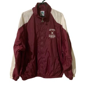 May include: Maroon and white athletic jacket with a full zipper and a high collar. The jacket has white sleeves and a maroon body. The text "COLD WEATHER CLASSIC CHAMPIONS 2000" is printed on the front.