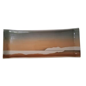 May include: Rectangular ceramic serving dish with a landscape design. The dish features a gradient of colors, including brown, orange, gray, and white. The design resembles a sunset over a body of water. The dish is approximately 12 inches long.