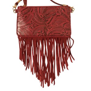 Puede incluir: Un bolso bandolera rojo con un dise&ntilde;o floral en relieve y largas flecos. El bolso tiene una correa desmontable y herrajes dorados. El bolso est&aacute; hecho de un material similar al cuero.