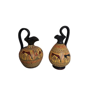 May include: Two antique-style ceramic vases with black handles and spouts. The vases have a yellow base with red and black geometric and animal designs. The handles curve upwards, and the spouts are flared.