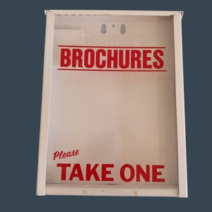 May include: White metal brochure holder with a clear front. The words "BROCHURES" and "TAKE ONE" are printed in red. The holder has two holes for hanging.