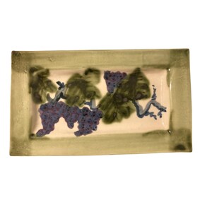 May include: A rectangular ceramic serving tray with a cream-colored center and a wide, sage green border. The center features a hand-painted design of purple grape clusters with dark green leaves and brown vine stems against a light background.