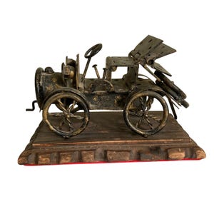 May include: A decorative metal sculpture of an antique car crafted from repurposed hardware components like nuts, bolts, and twisted wire. The vehicle features a black and gold finish, a steering wheel, and spoked wheels, mounted on a wooden base.