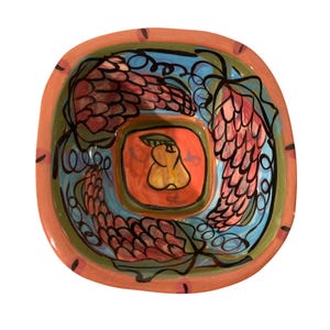 May include: A square ceramic serving bowl with a colorful, hand-painted design. The bowl features a peach-colored rim, a blue interior, and a central orange square with a pear illustration. The design includes pink and red floral elements.
