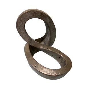 May include: A metallic sculpture featuring an infinity loop design with a textured, weathered bronze finish. The object consists of two interconnected oval-shaped rings that twist together to form a continuous, fluid, and three-dimensional shape.