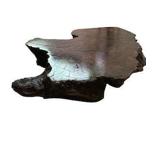 Puede incluir: Una losa de madera marrón oscuro de forma irregular con una superficie texturizada. La madera presenta grietas visibles y una forma natural, adecuada para exhibición decorativa o como pieza de servicio.