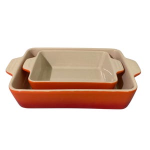 Puede incluir: Dos fuentes de horno de cerámica naranja, una dentro de la otra. La fuente más grande tiene forma rectangular con asas, y la fuente más pequeña también es rectangular. Ambas tienen un interior color crema.