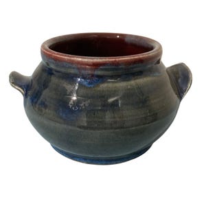 May include: A round ceramic pot with two small side handles, featuring a glossy glaze in shades of deep blue and grey. The interior of the pot is finished in a contrasting dark reddish-brown glaze that extends slightly over the top rim.