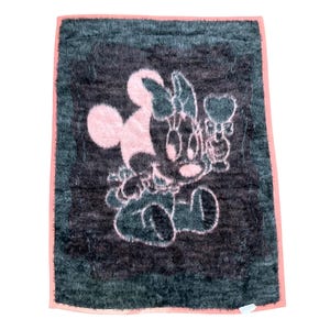 May include: A rectangular fuzzy blanket featuring a dark charcoal gray background with a light pink graphic of a cartoon mouse character holding a heart-shaped object. The blanket is finished with a solid light pink border along all four edges.