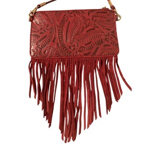 Puede incluir: Un bolso bandolera rojo con un dise&ntilde;o floral en relieve y largas flecos. El bolso tiene una correa de cadena dorada y un cierre de cremallera. El bolso est&aacute; hecho de un material similar al cuero.
