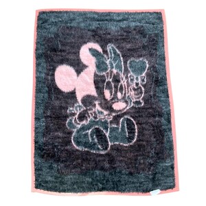 May include: A rectangular, fuzzy, dark gray blanket featuring a light pink graphic of a cartoon mouse character sitting and holding a heart-shaped object. The blanket is finished with a solid light pink border around the entire outer edge.