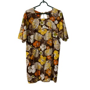 May include: A short-sleeved dress featuring a brown background with a repeating pattern of yellow and white pineapples and orange, yellow, and white hibiscus flowers. The dress has a round neckline with a small cutout detail at the upper back.