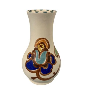 May include: A cream-colored ceramic vase with a flared rim featuring a dark teal dotted pattern. The body of the vase is decorated with a hand-painted floral motif in shades of deep blue, light blue, brown, and yellow, set against a smooth surface.