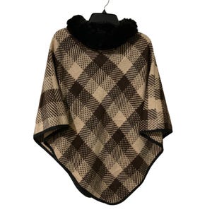 May include: A beige and dark brown plaid poncho featuring a thick black faux fur collar. The garment has a diamond-shaped checkered pattern throughout the fabric and is finished with a solid black trim along the bottom hem and edges.