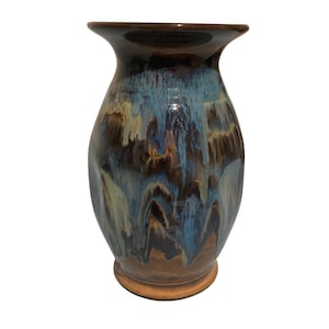 May include: A ceramic vase with a flared rim and a rounded body, featuring a glossy glaze in shades of deep brown, cream, and vibrant blue that drips down the surface in a vertical pattern, creating a multi-colored, layered effect.