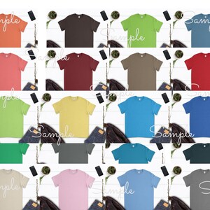 May include: A collection of 18 blank t-shirts in various colors, including coral, brown, maroon, yellow, green, blue, teal, gray, pink, and beige. The shirts are laid out on a white surface with a few decorative items around them.